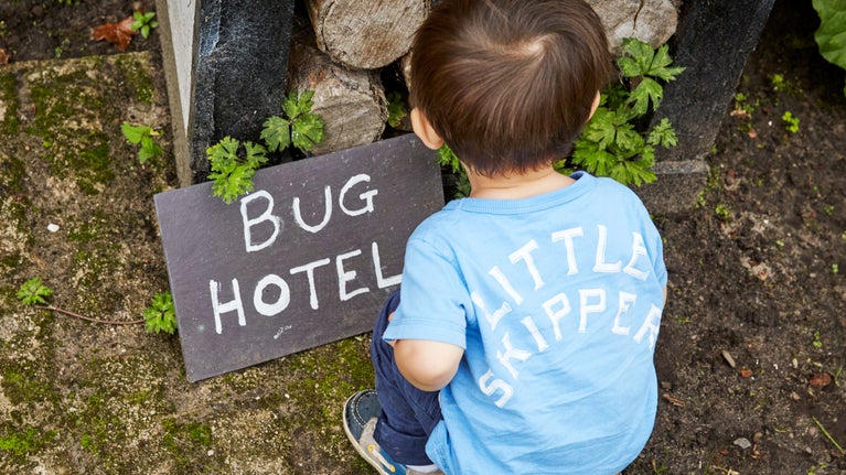 Child crouching in front of a bug hotel